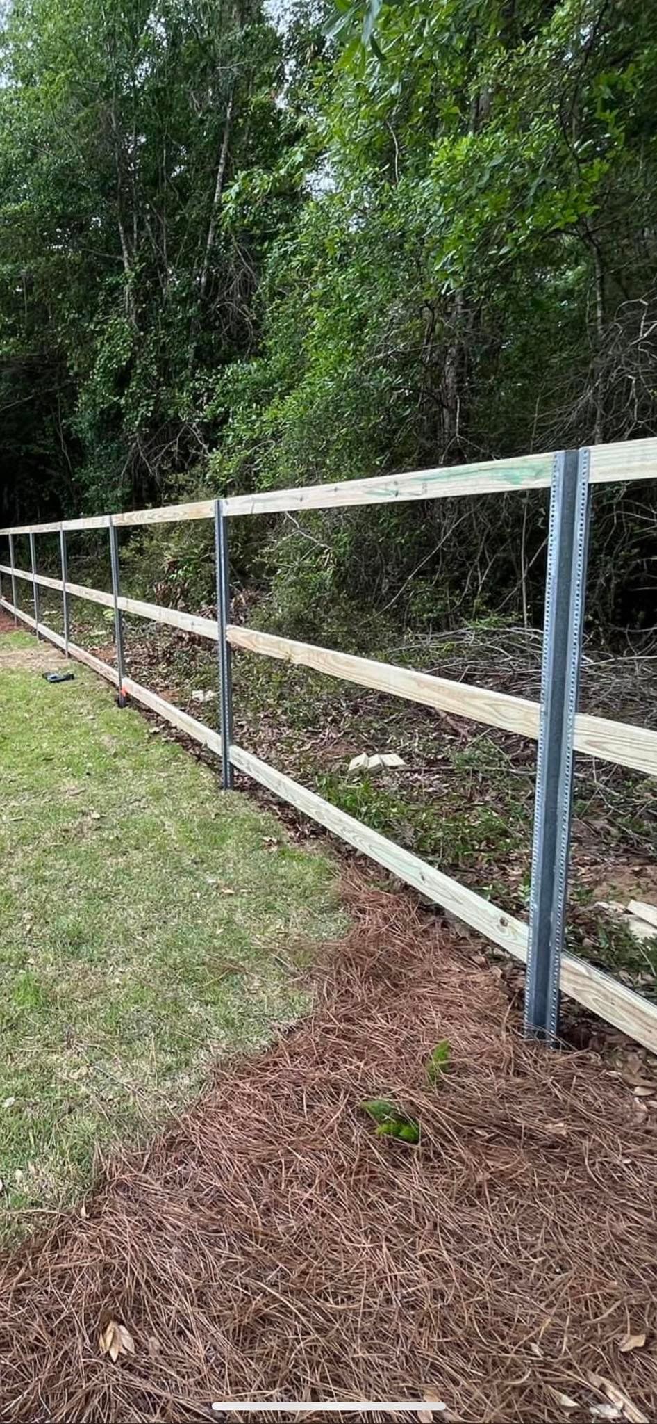 A white fence surrounds a grassy field with trees in the background.