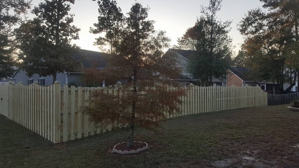 A wooden fence surrounds a yard with trees and a house in the background.