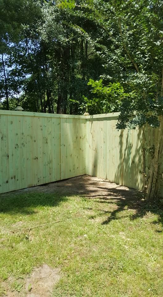 A wooden fence in a backyard with trees in the background.