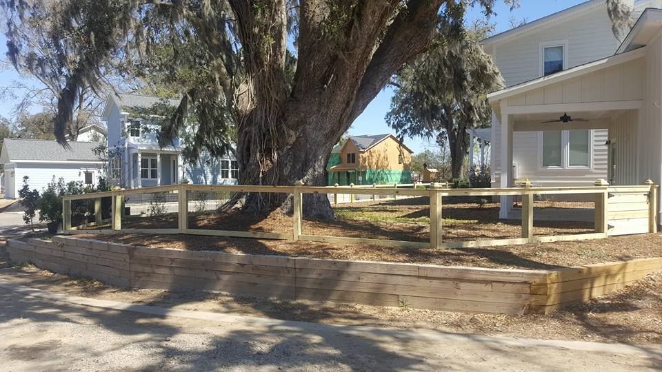 A wooden fence is surrounding a large tree in front of a house.