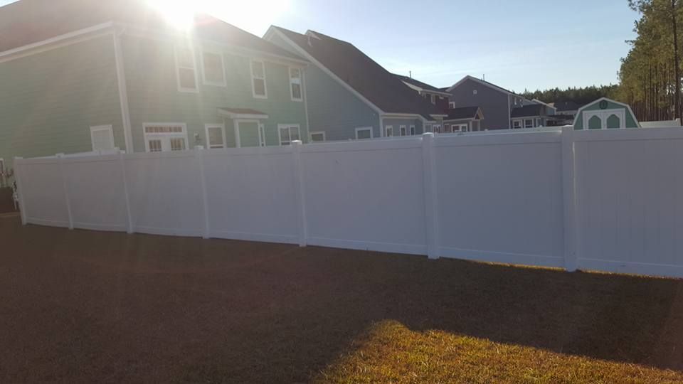 A white fence is in the backyard of a house.
