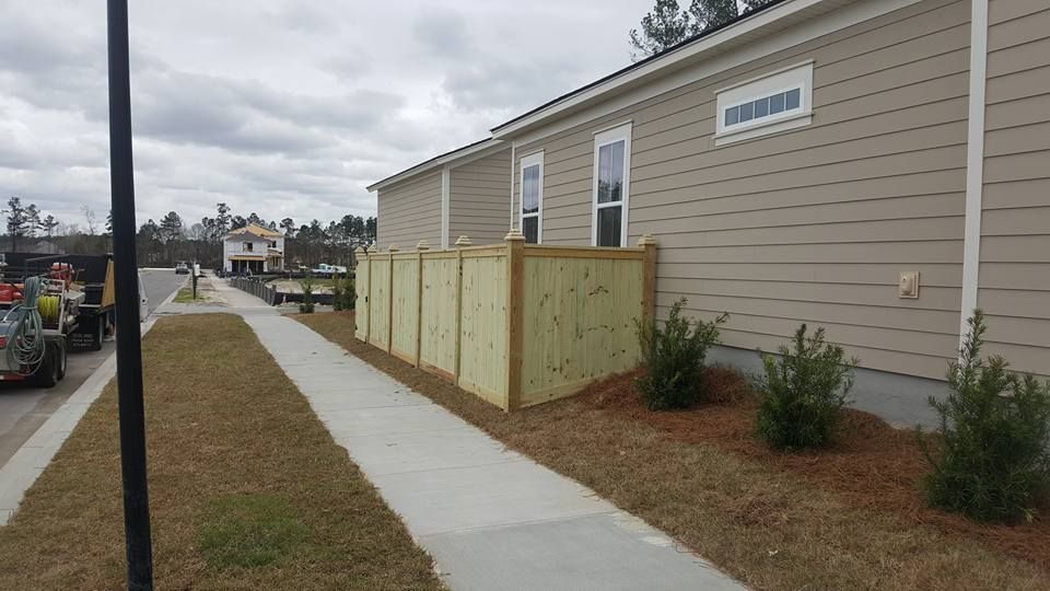 A wooden fence is along the sidewalk in front of a house.