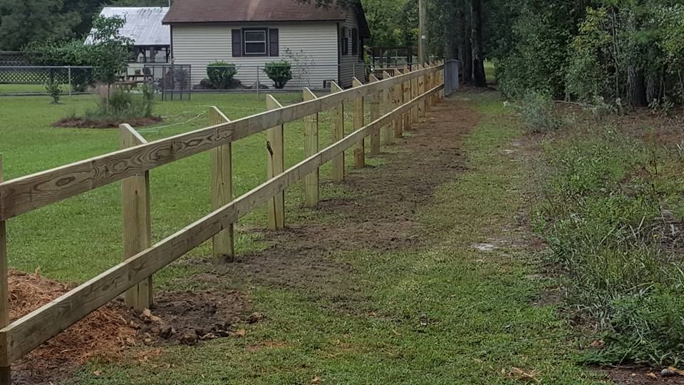 A wooden fence is sitting in the middle of a grassy field next to a house.
