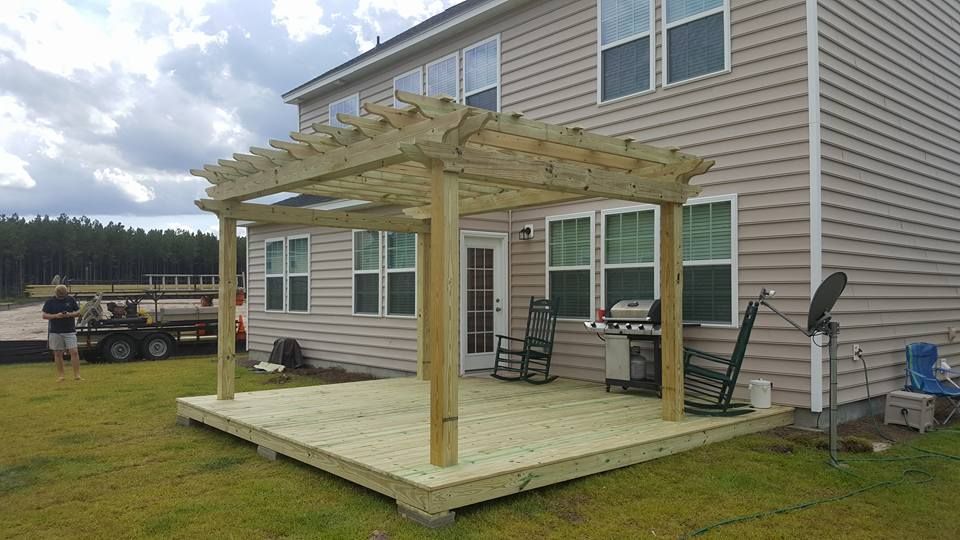 A wooden deck with a pergola and rocking chairs in front of a house.