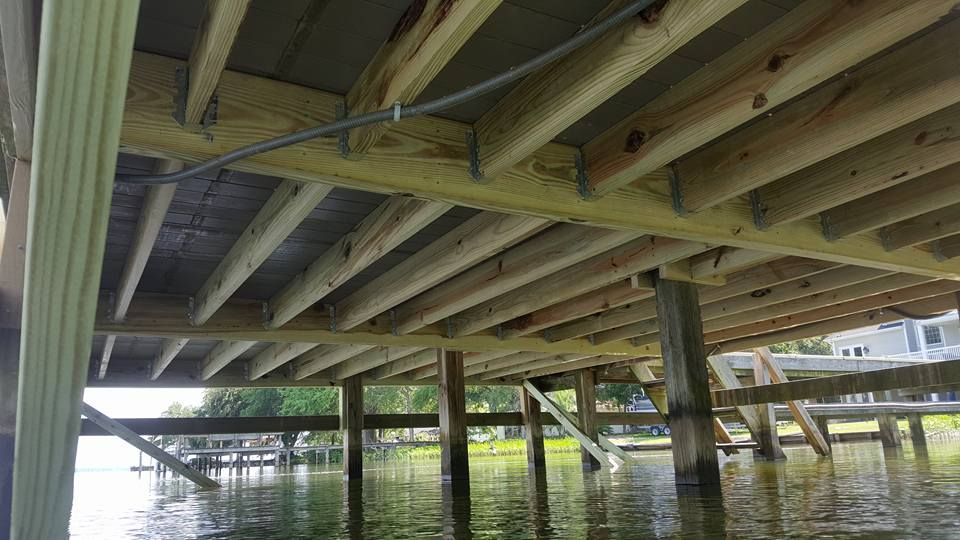 The underside of a wooden bridge over a body of water.