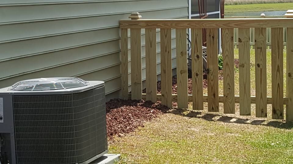 An air conditioner is sitting next to a wooden fence.