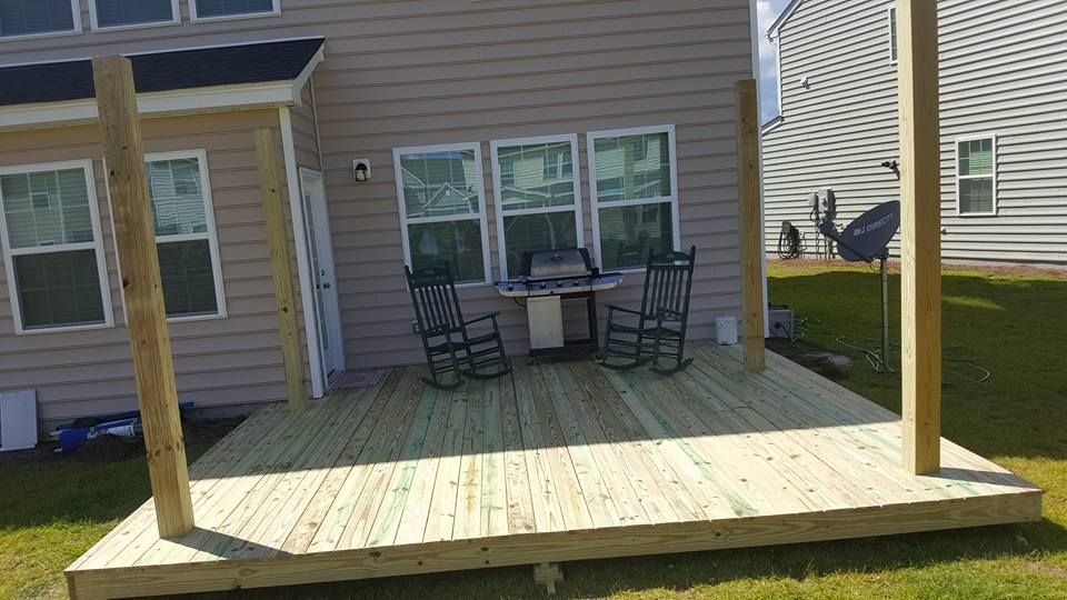 A wooden deck with rocking chairs and a table in front of a house.
