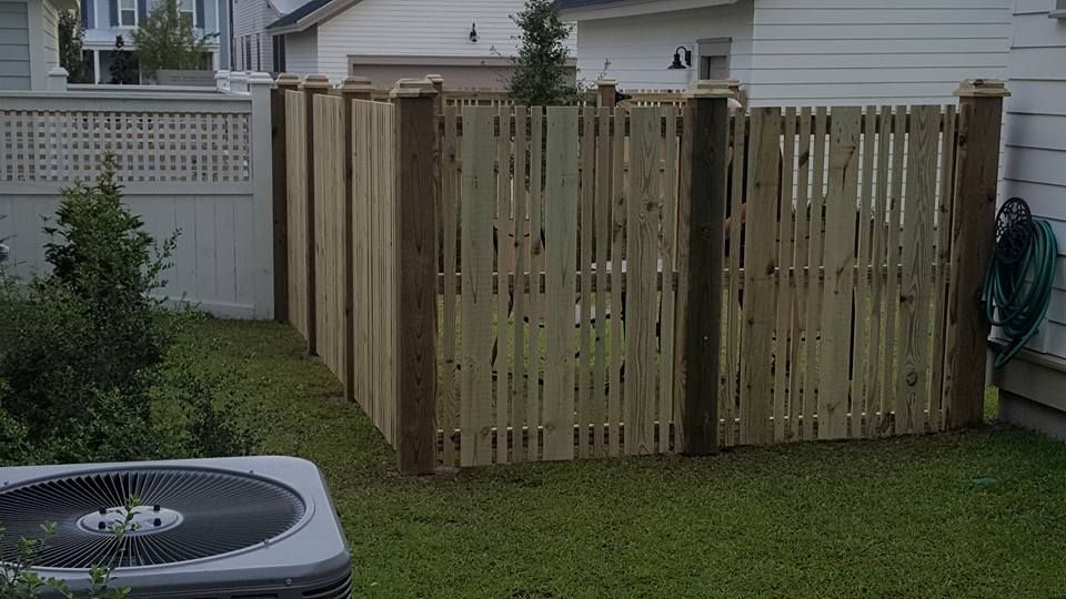 A wooden fence is in the backyard next to an air conditioner.