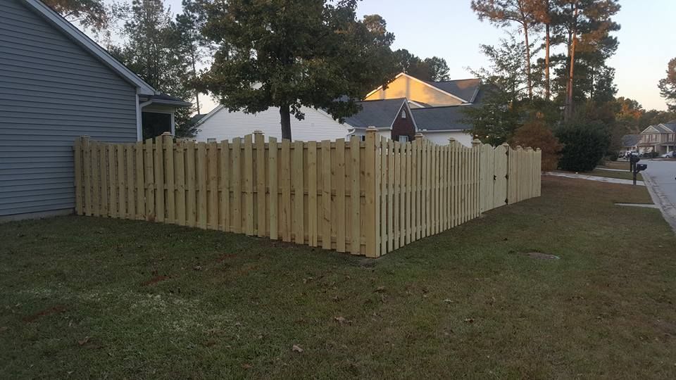 A wooden fence is in the middle of a yard next to a house.