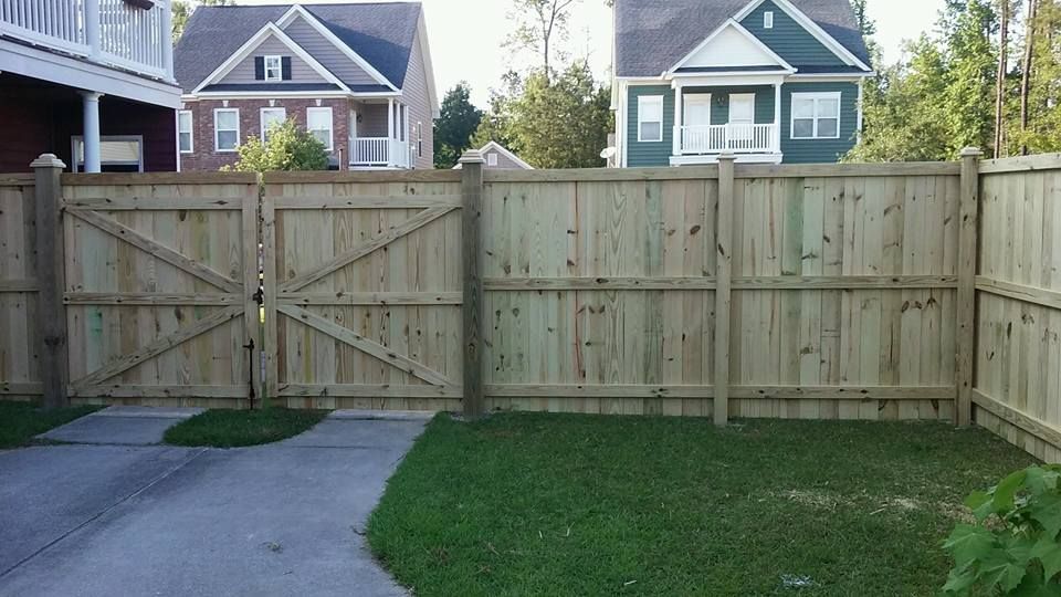 A wooden fence surrounds a driveway in front of a house.
