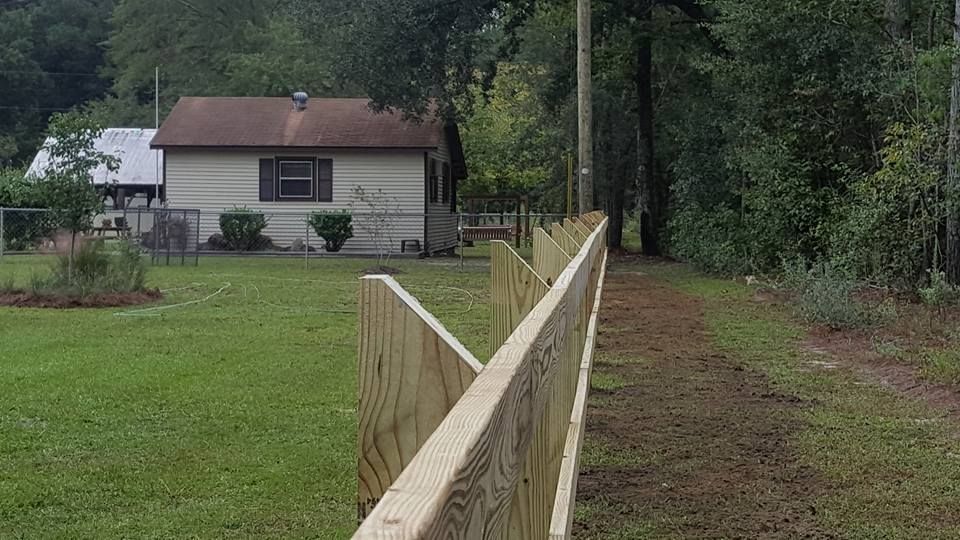 A wooden fence surrounds a grassy field in front of a house.