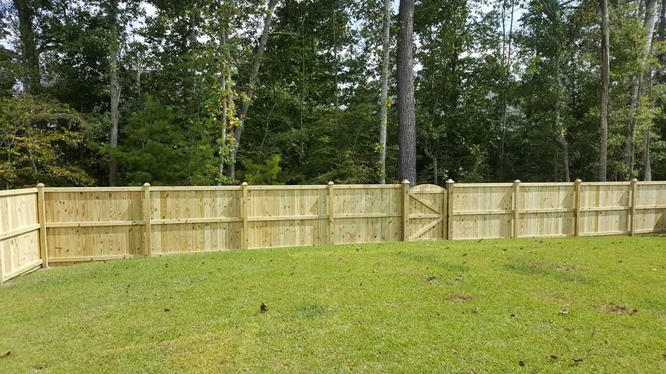A wooden fence surrounds a lush green yard with trees in the background.