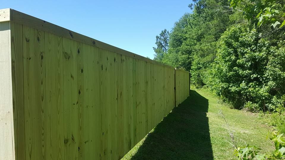 A long wooden fence is surrounded by trees and grass.