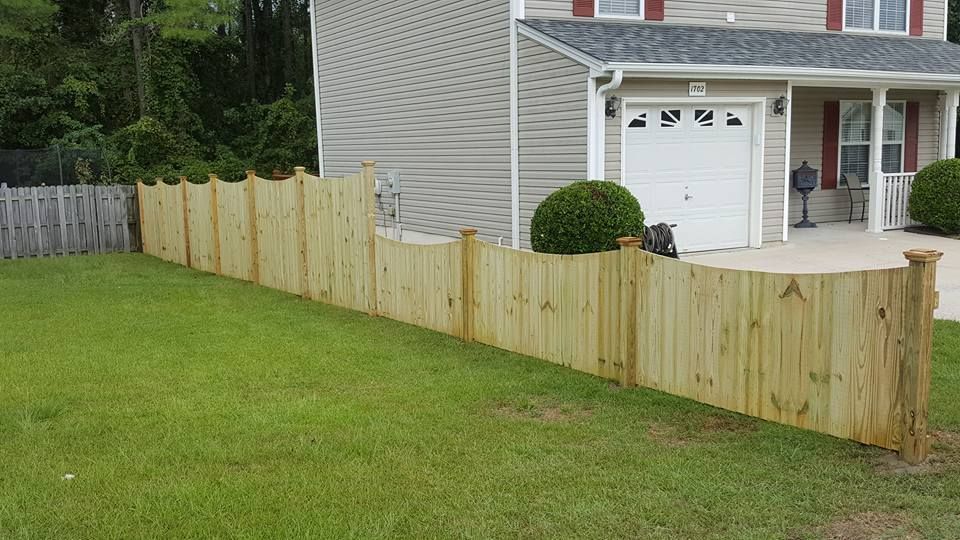A wooden fence is in front of a house with a garage.