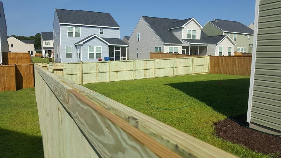 A wooden fence surrounds a yard with houses in the background