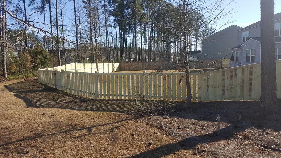 A wooden fence surrounds a yard with trees and a house in the background.