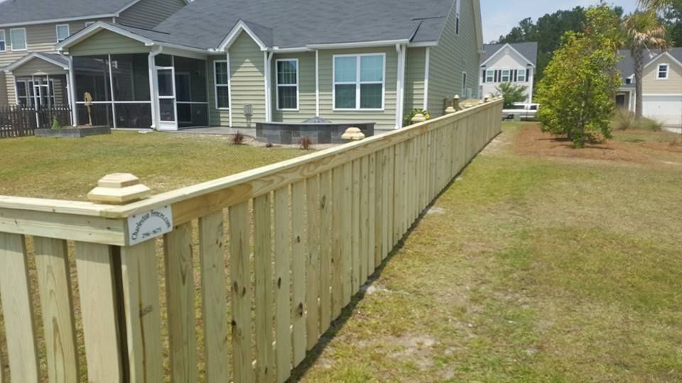 A long wooden fence surrounds a house in a residential area.