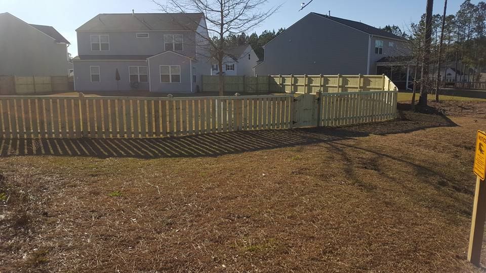 A wooden fence surrounds a yard with a house in the background.