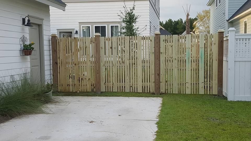 A wooden fence is surrounding a driveway in front of a house.