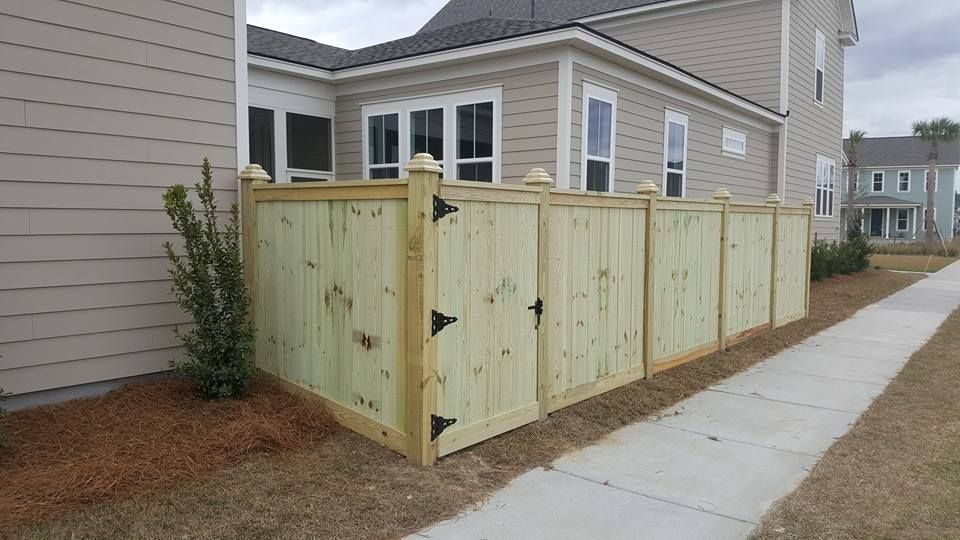 A wooden fence is sitting next to a sidewalk in front of a house.
