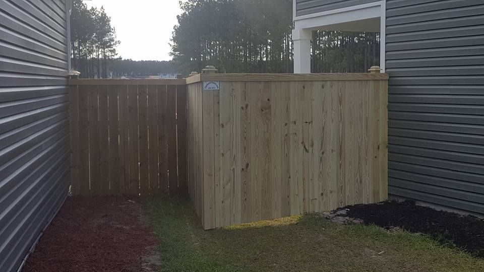 A wooden fence is between two houses in a backyard.