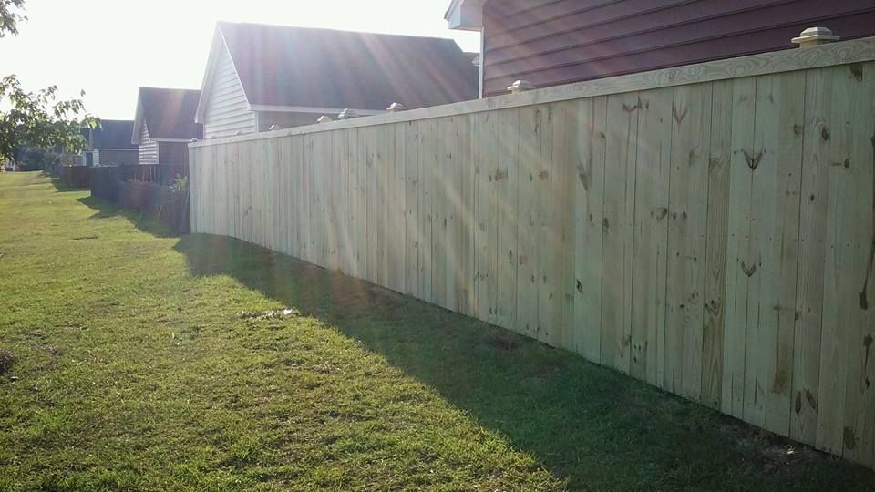 A wooden fence surrounds a lush green yard in front of a house.
