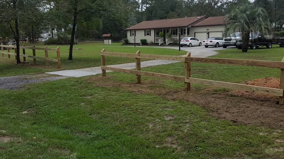 A wooden fence is in the middle of a lush green field in front of a house.