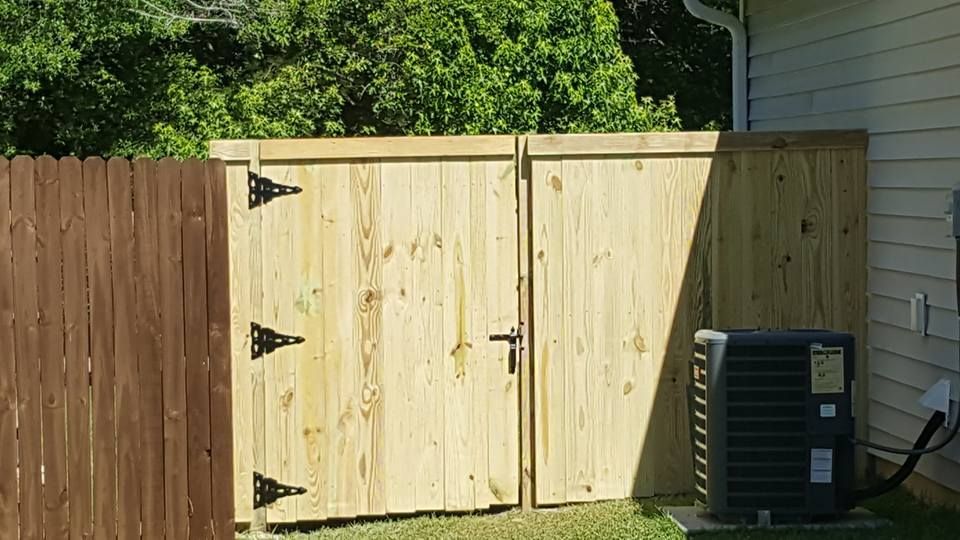 A wooden fence with two doors is next to a house with an air conditioner.