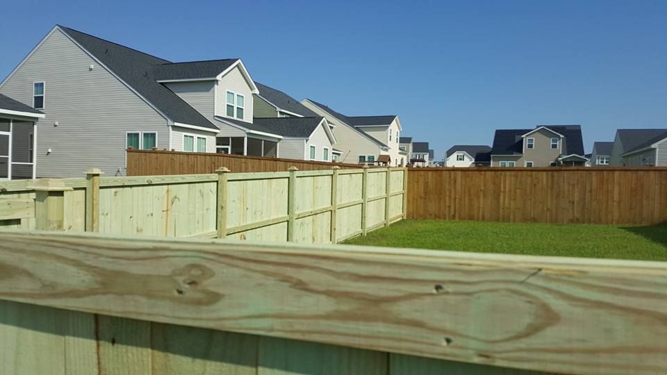 A wooden fence surrounds a yard with houses in the background