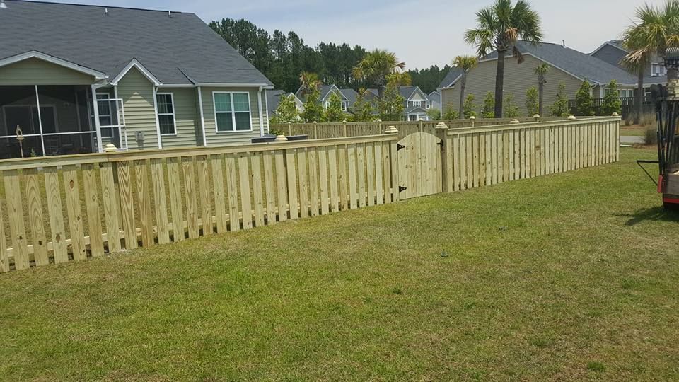 A wooden fence surrounds a lush green yard in front of a house.