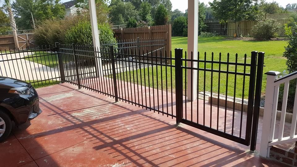A black car is parked in front of a wrought iron fence.