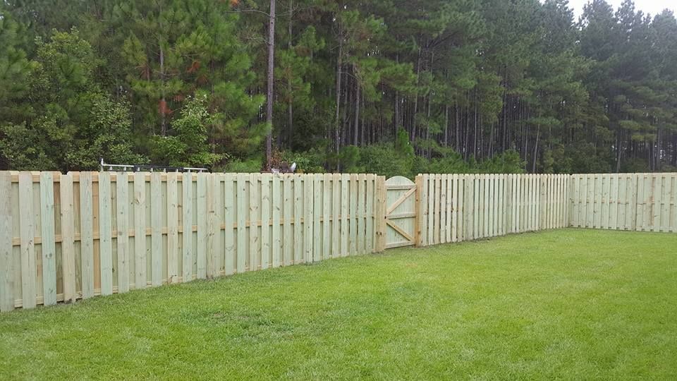 A wooden fence surrounds a lush green field with trees in the background.