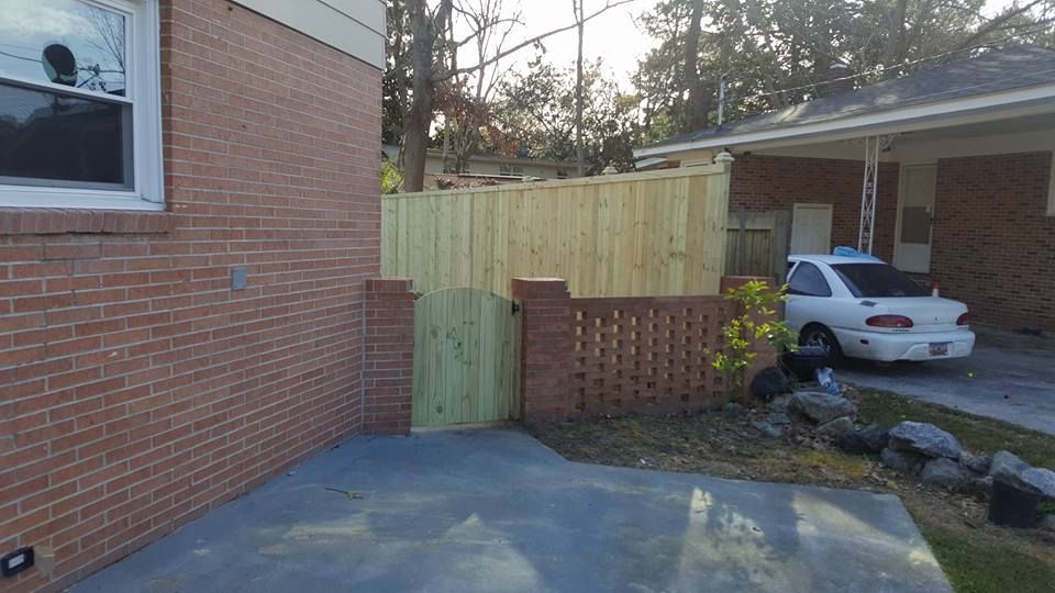A white car is parked in front of a brick house with a wooden fence.