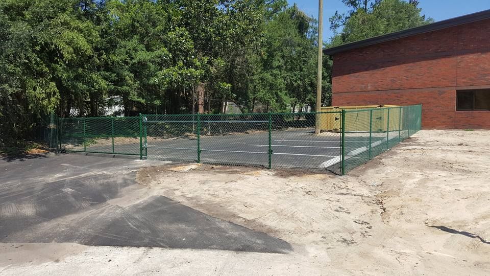 A green fence surrounds a parking lot in front of a brick building.