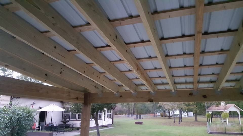 A wooden structure with a metal roof and a house in the background