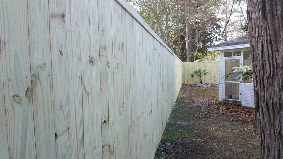 A wooden fence is surrounding a house in a backyard.