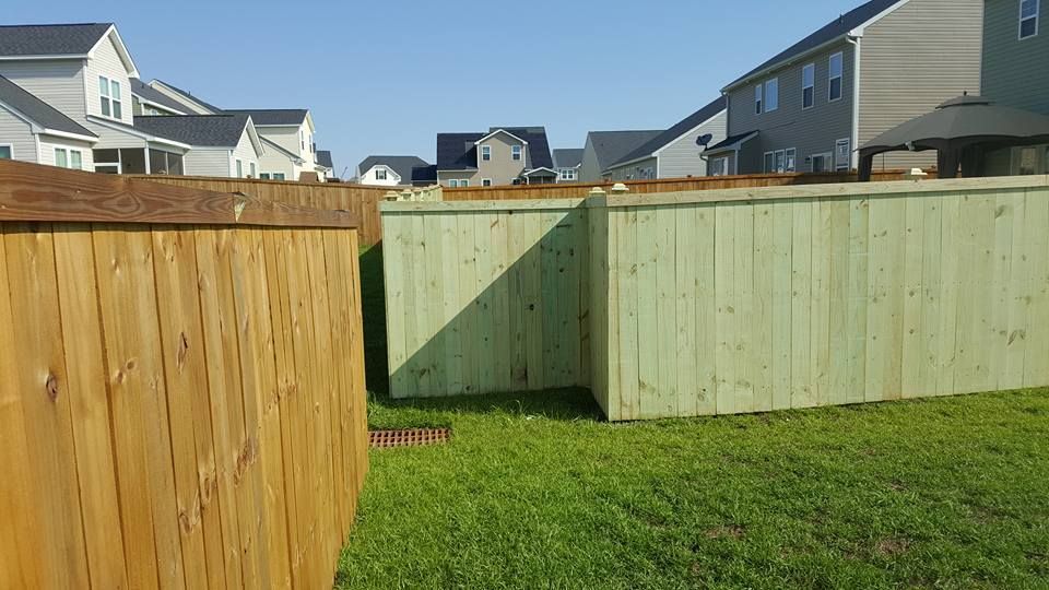 A wooden fence in a backyard with houses in the background.