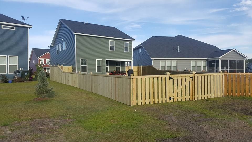 A wooden fence surrounds a backyard with houses in the background.