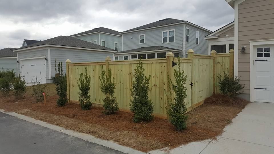 A wooden fence is in front of a house in a residential area.