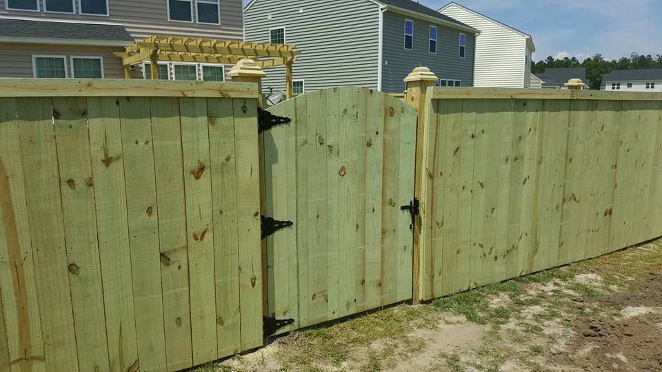 A wooden fence with a gate and a pergola in front of a house.
