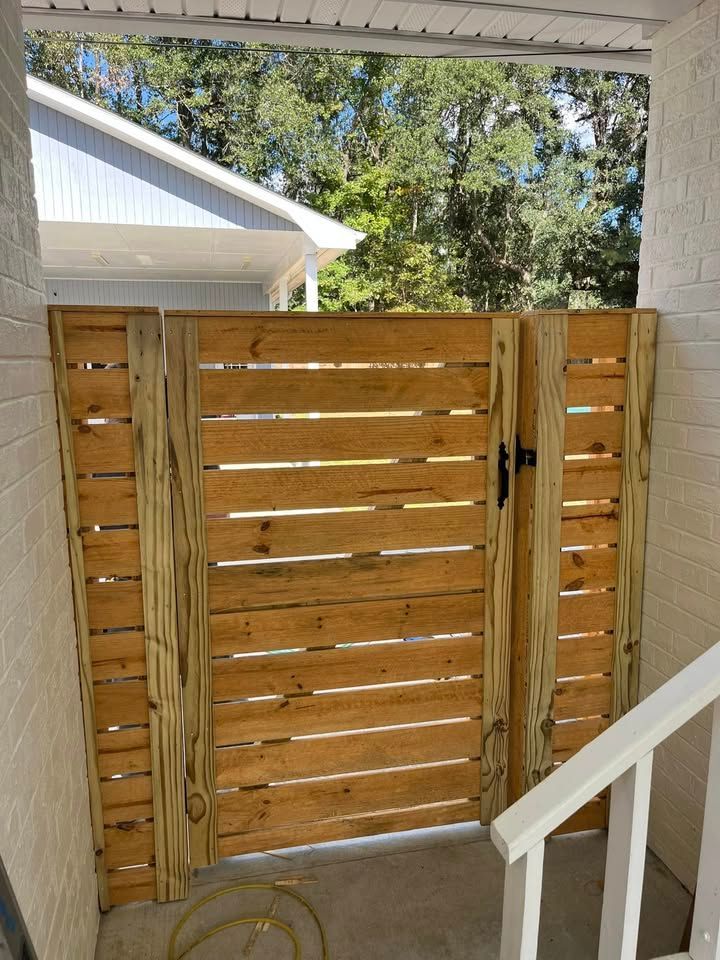 A wooden gate is sitting on the side of a white brick building.