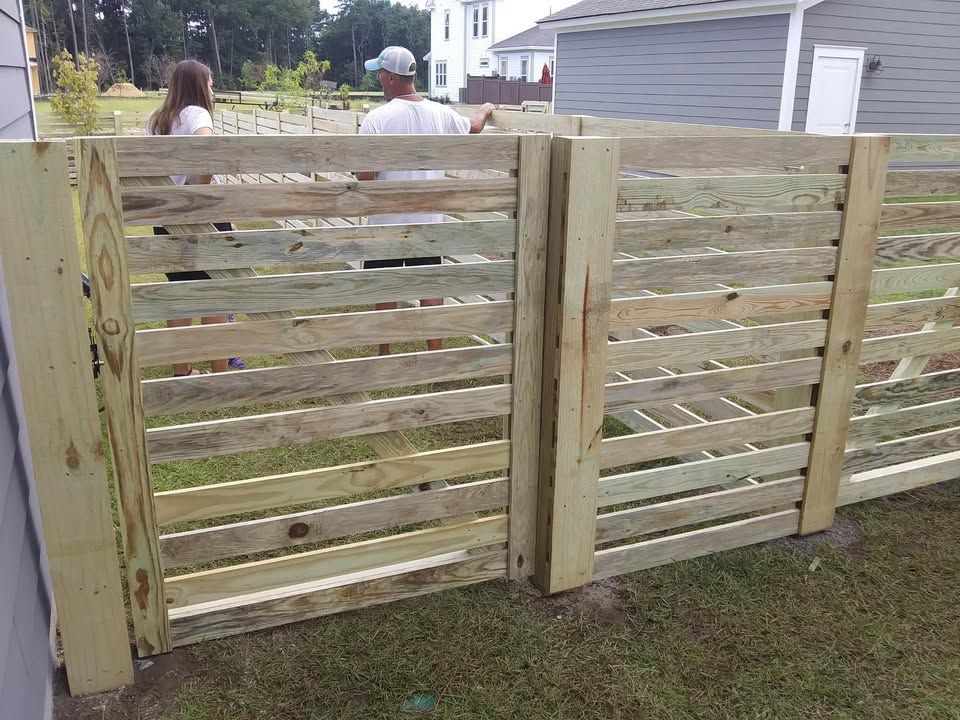 A man and a woman are standing behind a wooden fence.