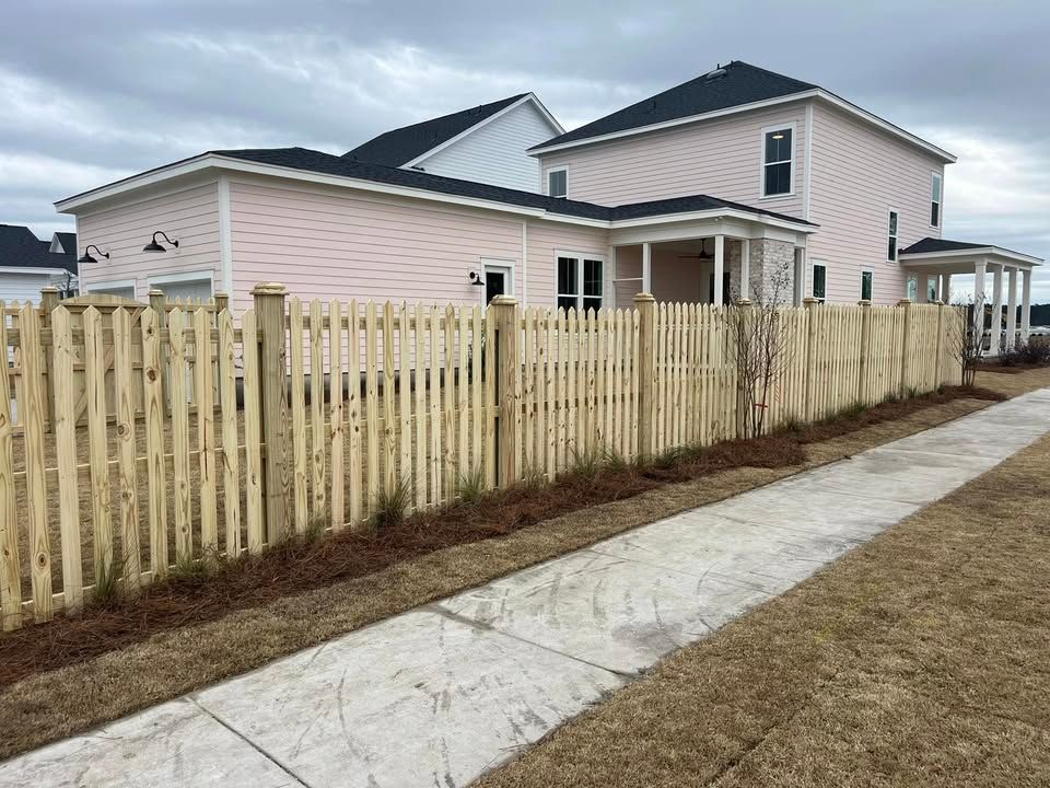 A wooden picket fence surrounds a large pink house.