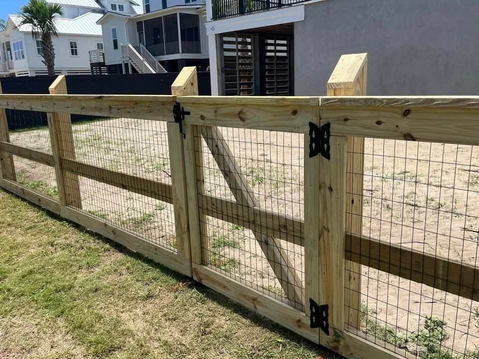 A wooden fence with a chicken wire gate in front of a house.