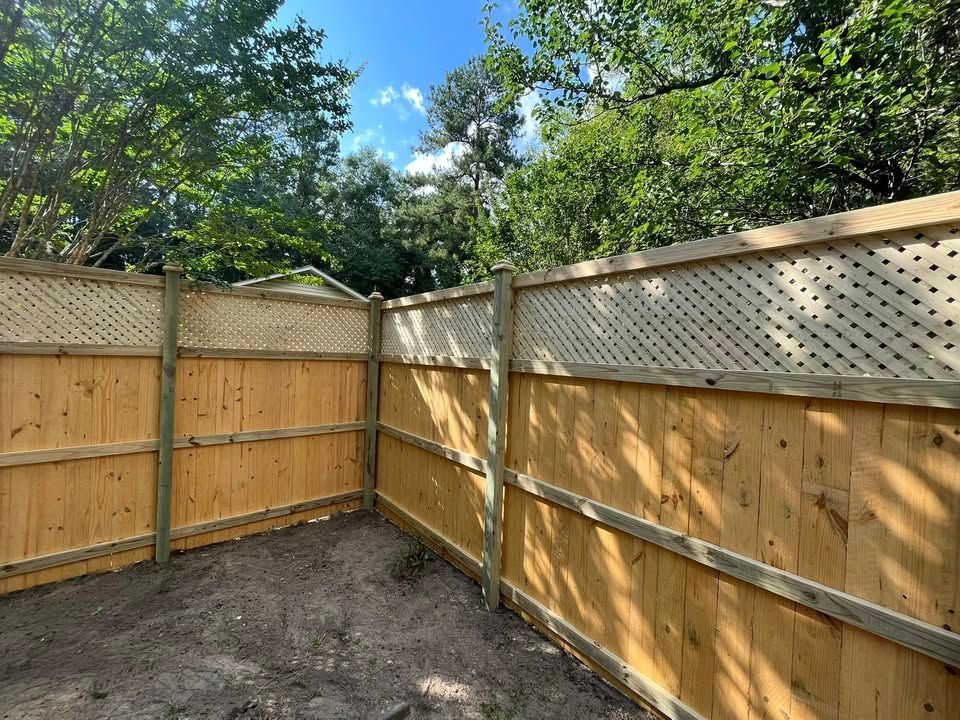 A wooden fence with a lattice in the middle is surrounded by trees.