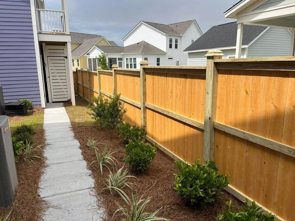 A wooden fence surrounds a lush green garden in front of a house.