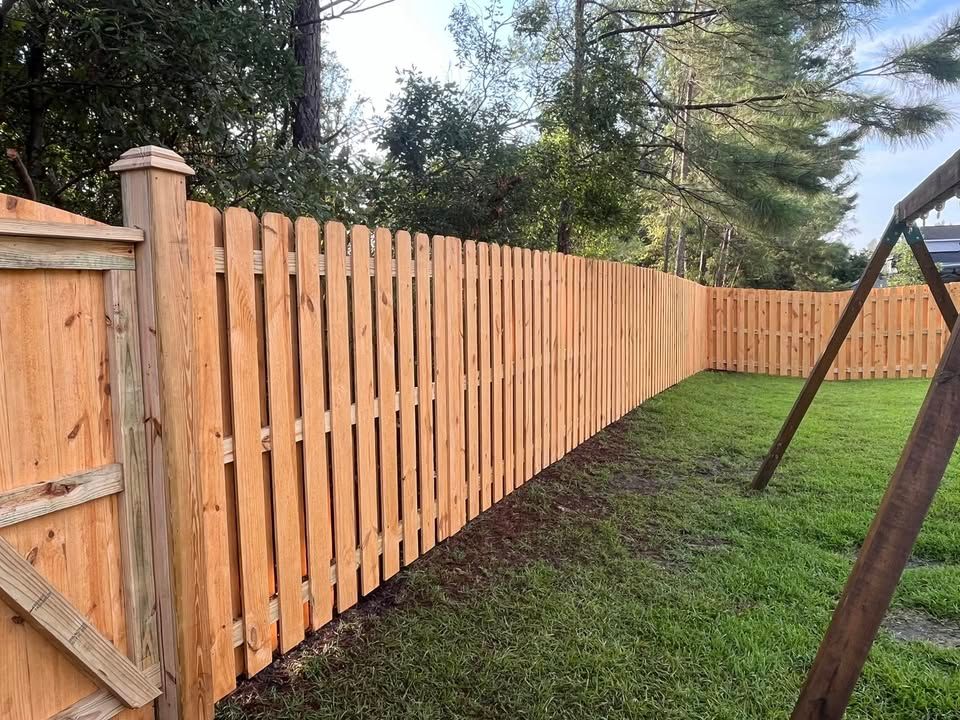 A wooden fence in a backyard with a swing set in the background.