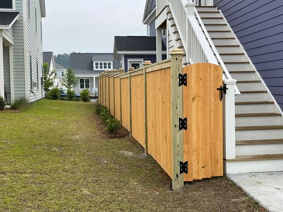 A wooden fence with a gate in front of a house with stairs.