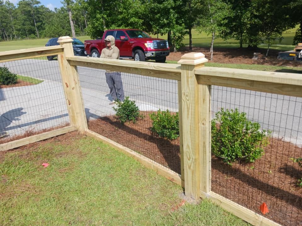 A man is standing next to a wooden fence with a red truck in the background.