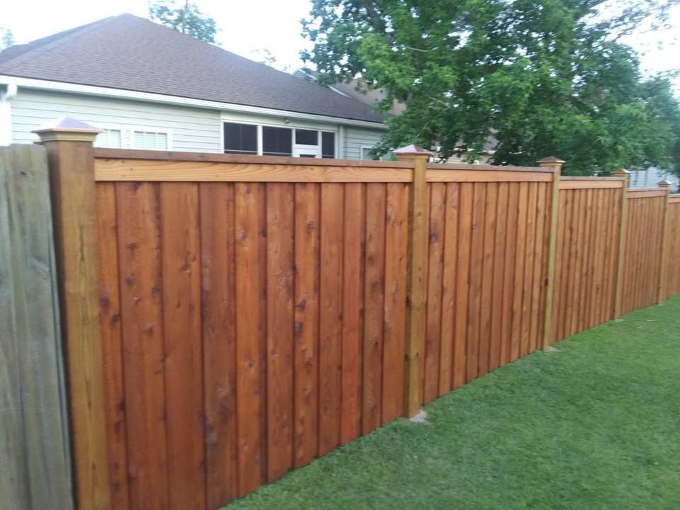 A wooden fence surrounds a lush green yard in front of a house.